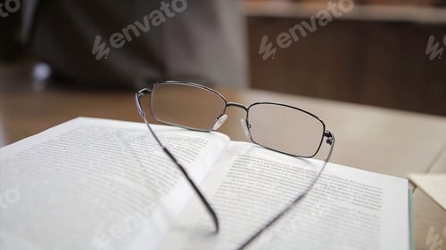Preview: Eyeglasses and Open Book on Wood Table