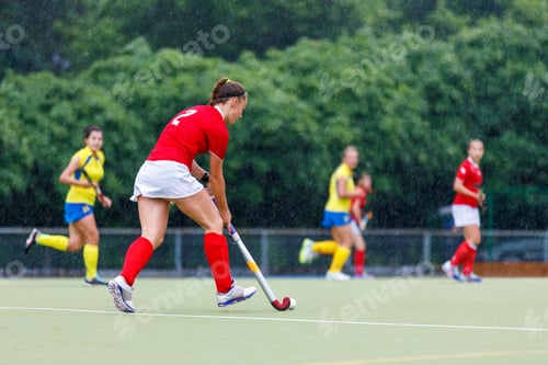 Preview: Young sportswoman playing field hockey under the rain.