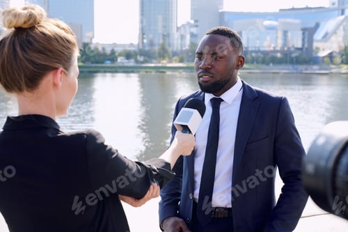 Preview: Young African entrepreneur standing in front of female reporter or journalist with microphone