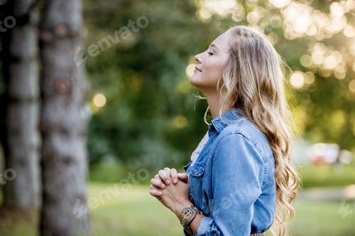 Preview: Woman in a blue dress praying in the garden under the sunlight with a blurry background