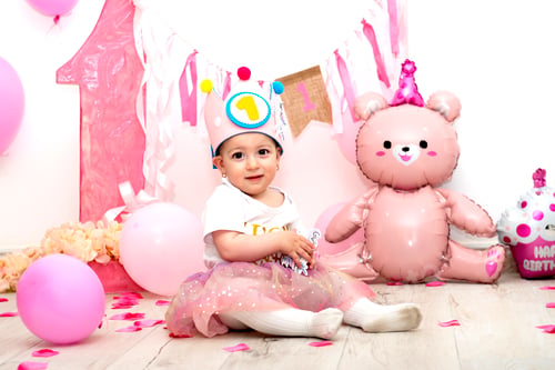 Preview: Little child in a crown with in festive clothes among festive balls, ribbons, number 1. Celebrating