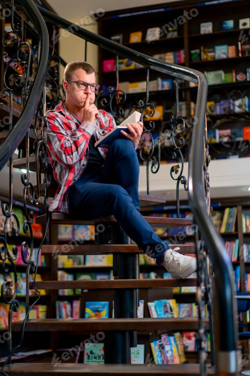 Preview: a man in glasses sits on the stairs in the library carefully reads a book and worries its characters