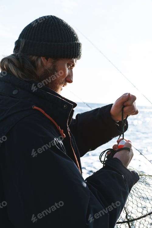 Preview: Handsome young man fisherman wearing coat and hat at the seashore.