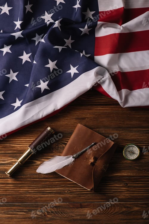 Preview: top view of leather notebook, nib, telescope and compass on wooden surface with American national