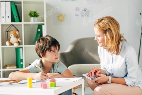 Preview: kid with dyslexia holding pencil and smiling child psychologist talking to him