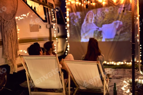 Preview: Young cheerful people watching a movie on camping site