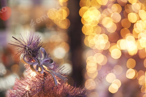 Preview: Stylish purple christmas tree with bow on background of golden lights illumination bokeh. Magic time