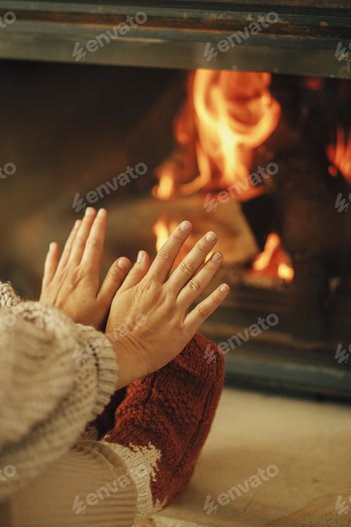 Preview: Woman in cozy socks warming up feet and hands at fireplace. Heating house with wood burning stove