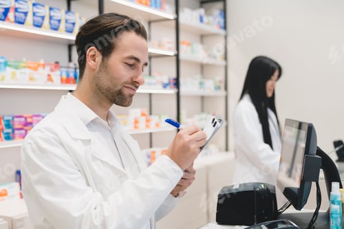 Preview: Pharmacists working at cash point desk in drugstore using computer and writing on clipboard