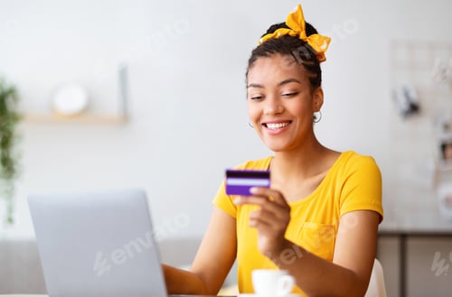 Preview: Black lady using laptop computer and credit card at home