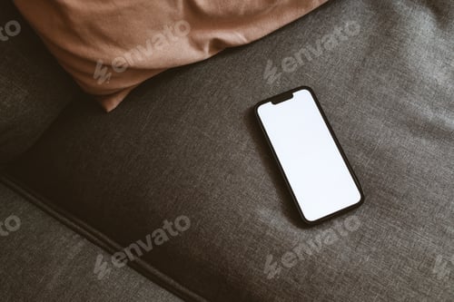 Preview: Smart mobile phone device with blank white mockup screen on living room sofa