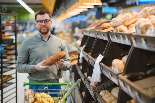 Preview: man chooses a fresh bread loaf in the supermarket, in grocery store.
