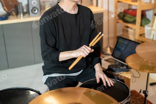 Preview: Guy in black sweatshirt and jeans holding drumsticks over drum while touching it