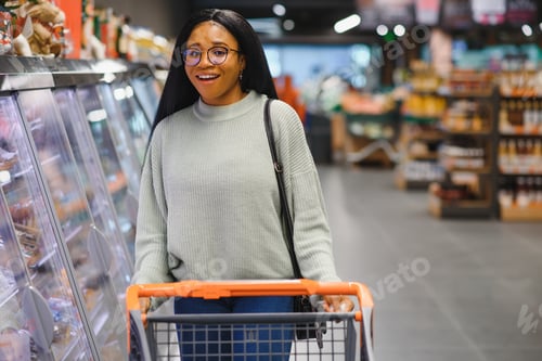 Preview: African american woman with shopping cart trolley in the supermarket store look on mobile phone