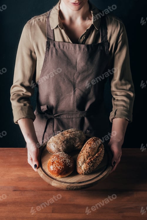 Preview: partial view of woman holding loafs of bread on wooden cutting board isolated on black