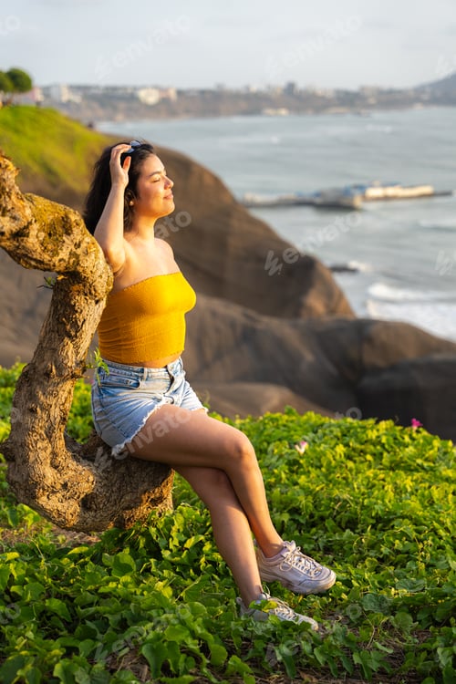 Preview: Young woman relaxing on a cliffside at sunset after work