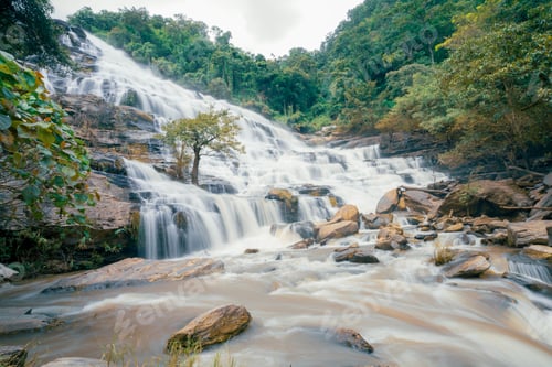 Preview: Beautiful waterfall with a lush green forest in the background The water is flowing down the rocks