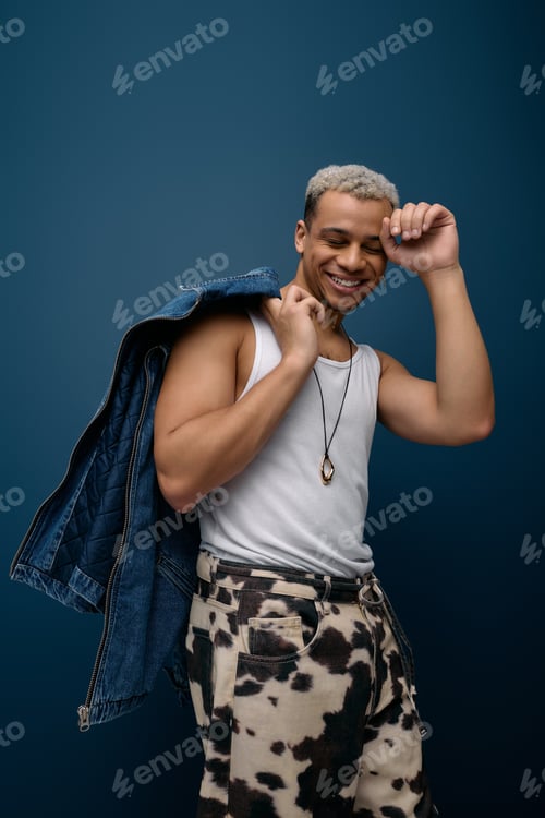 Preview: Young man showcases vibrant style in denim jacket against blue backdrop