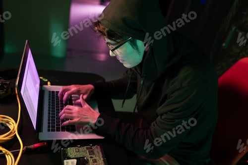Preview: Asian male hacker using a laptop in computer server room