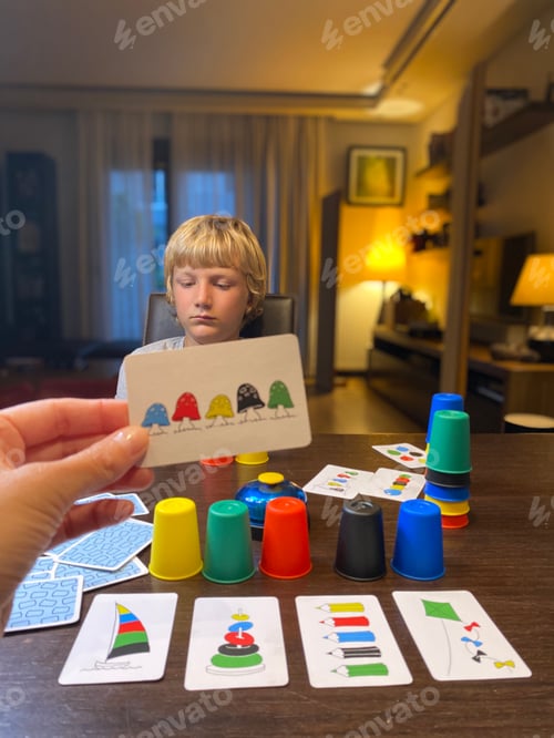 Preview: Game night, blond 9 years old boy playing with hiscmother board game, smiling, cozy dark room