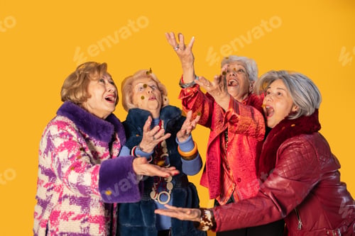 Preview: Group of senior women catching falling confetti on yellow background