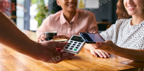Preview: Woman In Coffee Shop Paying Bill With Contactless Mobile Phone Payment