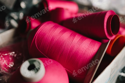 Preview: Thread spools stand on table in clothing workshop, ready for sewing and garment creation.