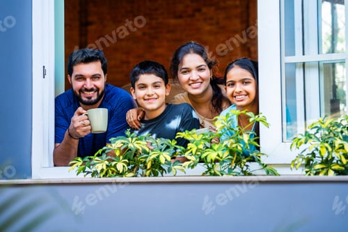 Preview: Happy Indian parents and children pointing and smiling while watching city view indoors