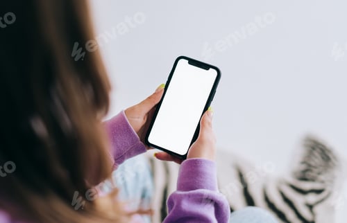 Preview: Woman holding a smartphone with a white screen mock up, resting on a sofa in living room at home.