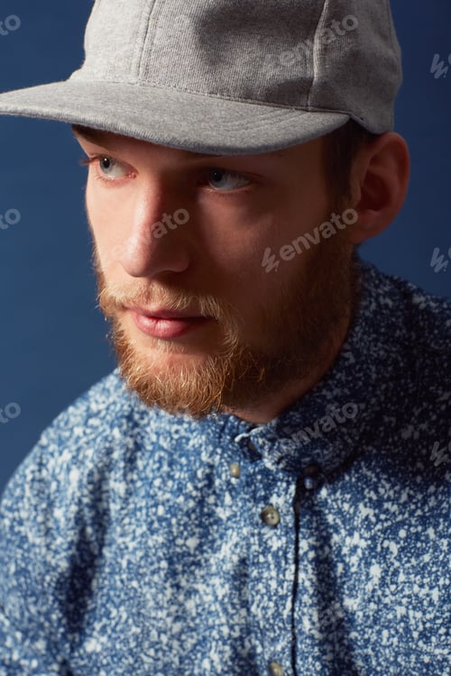 Preview: Thinking it over. A young man with a beard and unique sense of style looking away.