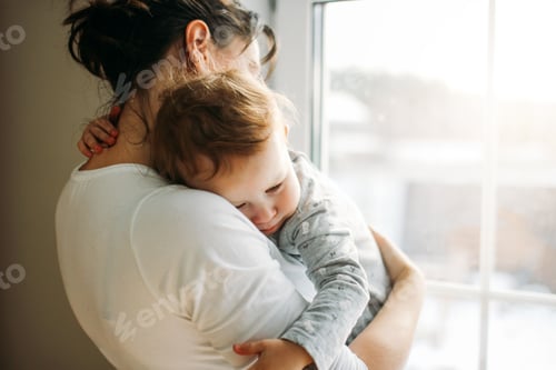 Preview: Young womanwith baby girl on hands near window at home