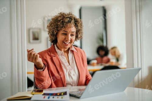 Preview: Happy businesswoman working on laptop in modern office with colleagues in background