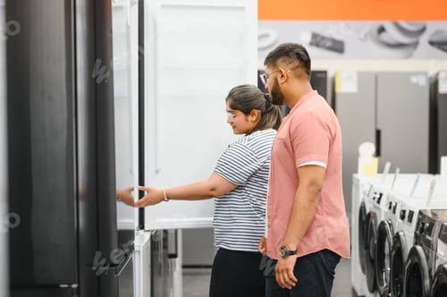 Preview: Young indian couple, satisfied customers choosing fridges in appliances store