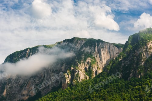 Preview: Rocky mountain range with trees and clouds