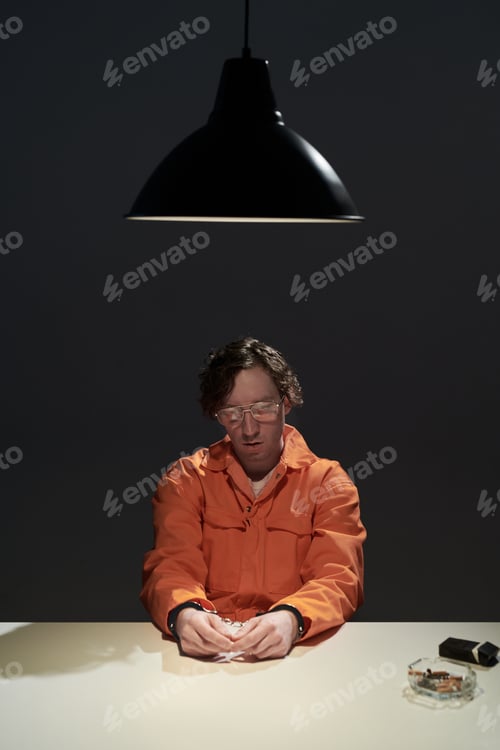 Preview: Illuminated Man in Orange Attire Sitting Under Hanging Lamp