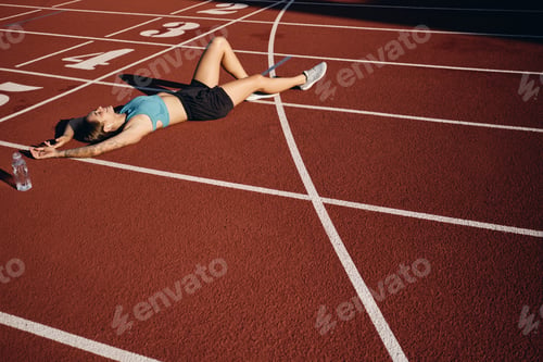 Preview: Tired smiling athlete girl in sportswear joyfully lying on runner track after workout on stadium