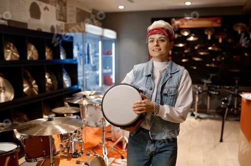 Preview: Young hipster woman choosing drum unit at musical shop feeling satisfaction
