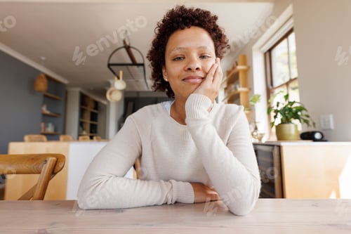 Preview: Non-binary person sitting at wooden dining table in home kitchen with knit sweater and potted plant