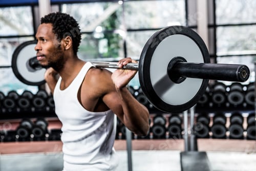 Preview: Muscular man exercising with barebell at gym