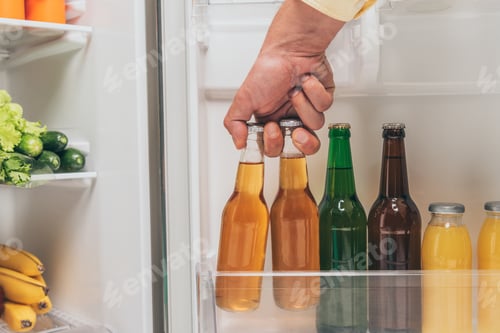 Preview: cropped view of man taking bottles of beer out from open fridge with fresh food on shelves