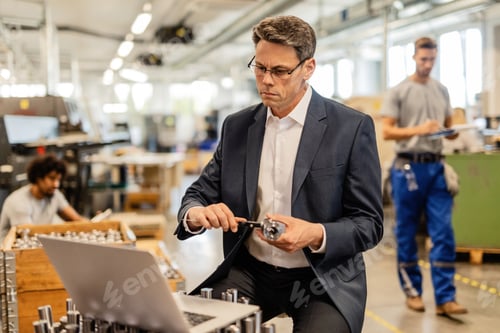 Preview: Male engineer using computer while taking measurements of steel cylinder with a caliper.