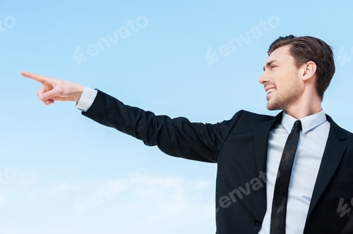 Preview: There... Side view of a young businessman pointing at copy space against blue sky