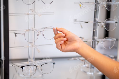Preview: Close up hand of young people select glasses on shelf in optical shop.