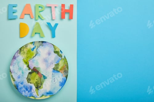 Preview: top view of colorful paper letters and planet picture on green and blue background, earth day