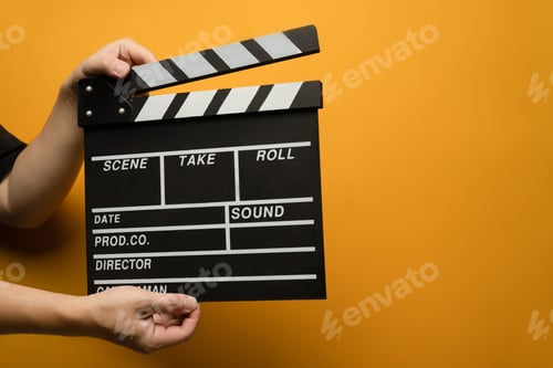 Preview: Hands holding black clapperboard on yellow background.