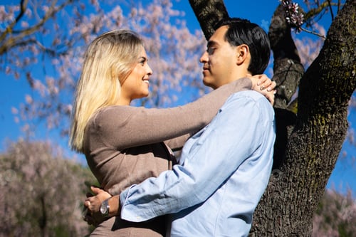 Preview: Happy couple embracing under blooming trees in springtime sunlight