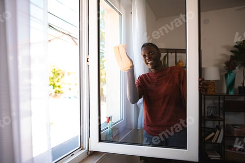 Preview: Young man cleaning windows at home smiling and looking outside