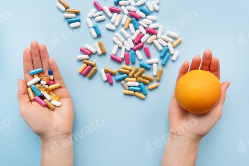 Preview: Many multi-colored pills, man's hands in one vitamins in another fresh orange.