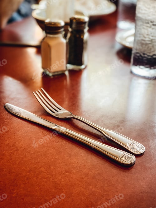 Preview: Silverware, salt and pepper shakers and glasses on a burnt orange diner tabletop