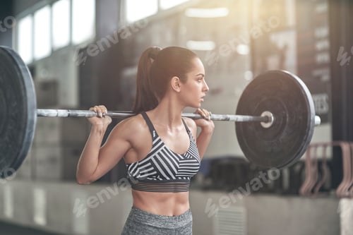 Preview: Young woman exercises in gym healthy lifestyle ready to lift bar